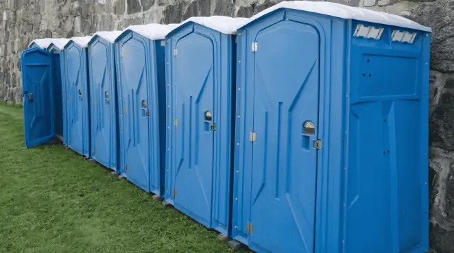 Row of blue portable toilets lined up on grass against a stone wall for event sanitation in ,